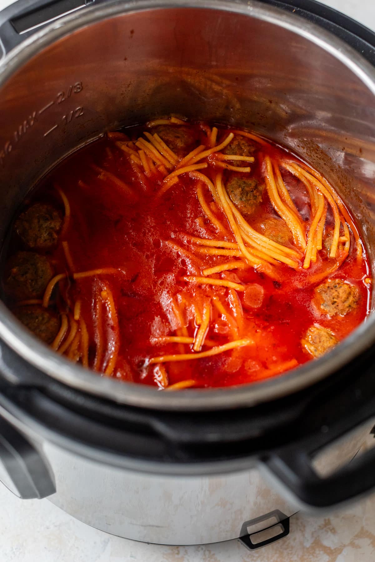 side view of cooked spaghetti noodles, meatballs, and tomato sauce in an instant pot.