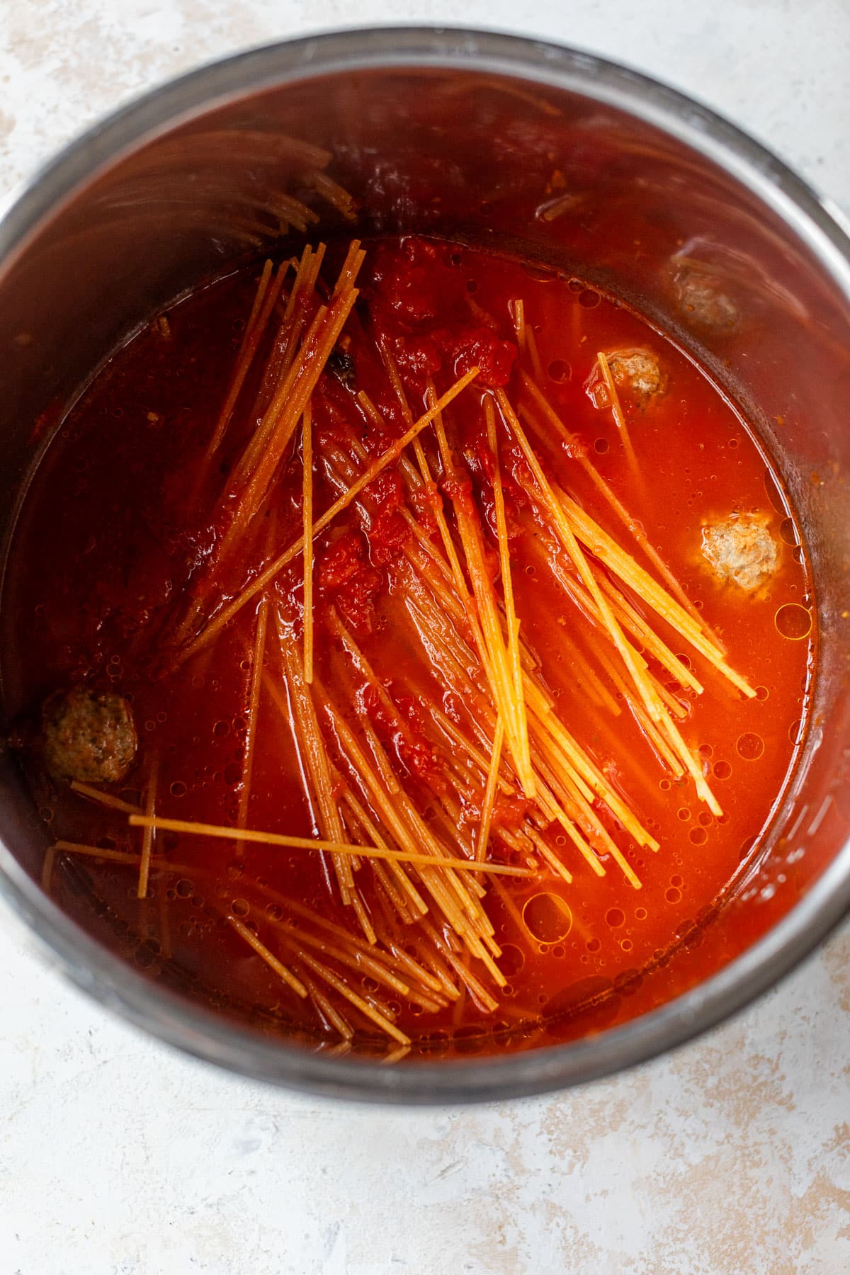 overhead view of uncooked spaghetti noodles, meatballs, and tomato sauce in an instant pot.