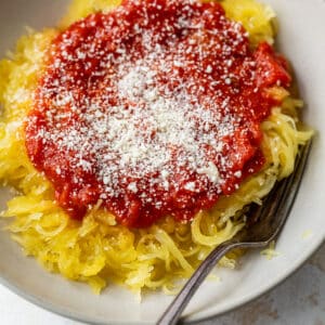overhead view of cooked spaghetti squash stands topped with tomato sauce and parmesan in a bowl with a fork.
