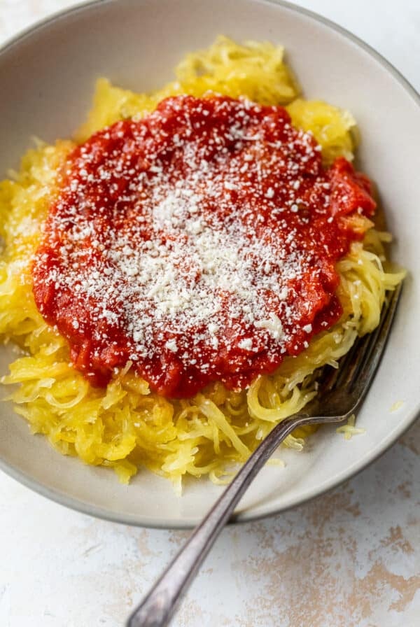 overhead view of cooked spaghetti squash stands topped with tomato sauce and parmesan in a bowl with a fork.