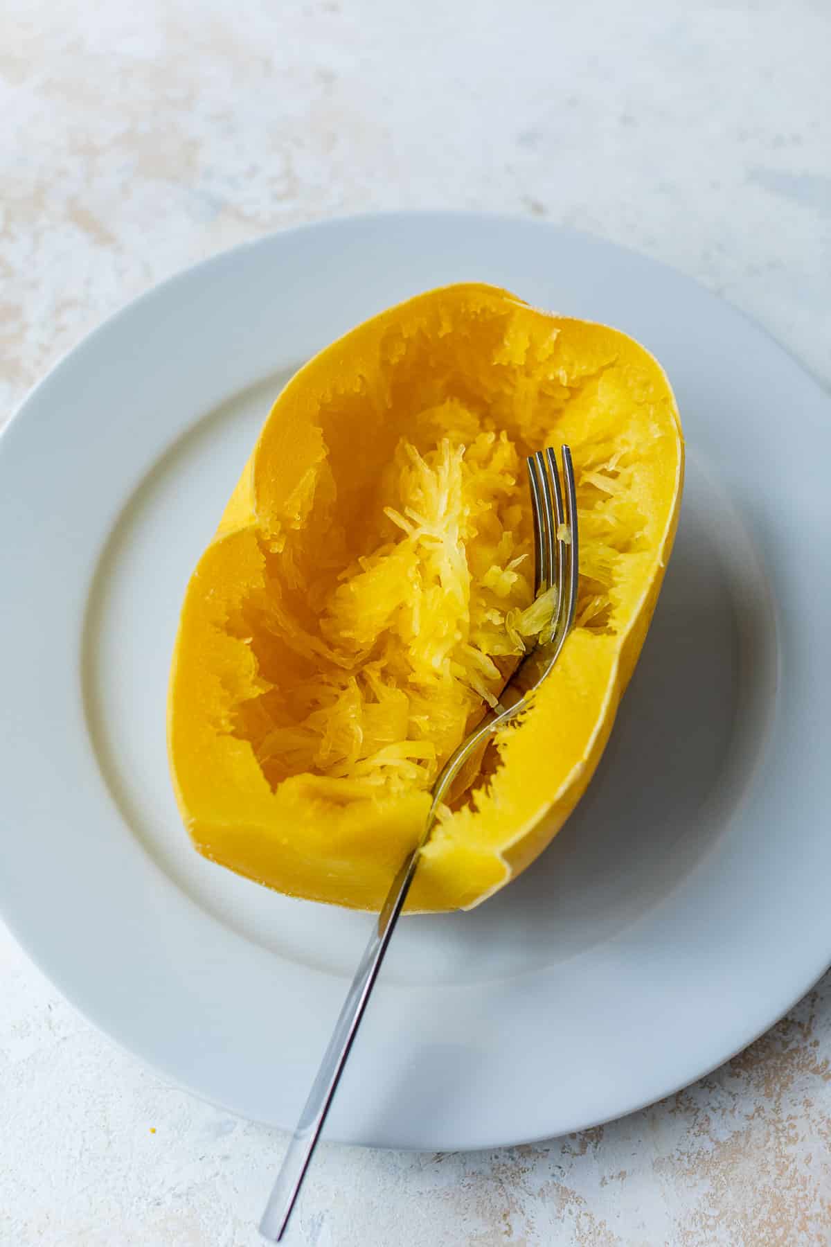 side view of a fork scraping a halved spaghetti squash on a white plate.