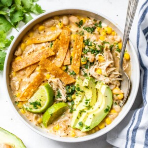 bowl of soup topped with avocado, cilantro and tortilla strips