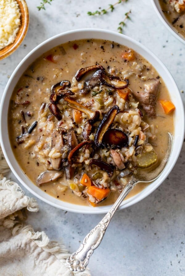 a bowl of mushroom rice soup with a spoon in it beside a small bowl of grated parmesan cheese