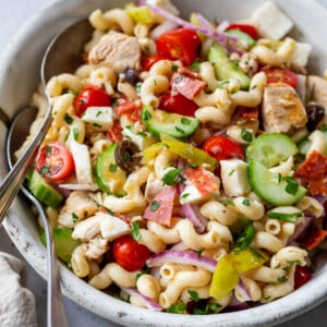 Italian pasta salad with two spoons in a large white bowl.