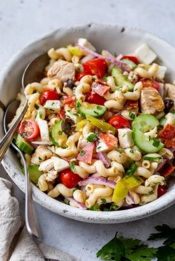 Italian pasta salad with two spoons in a large white bowl.