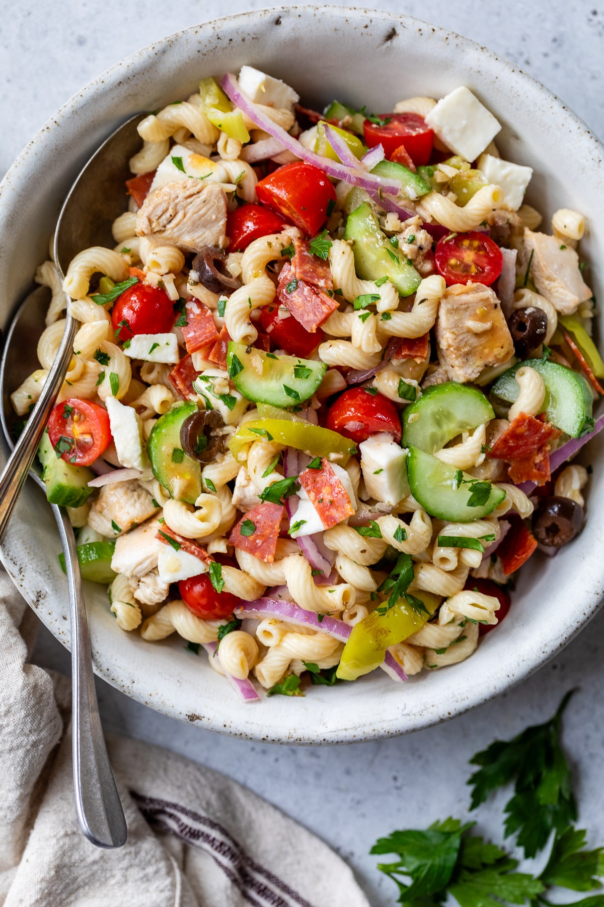 Italian pasta salad with two spoons in a large white bowl.