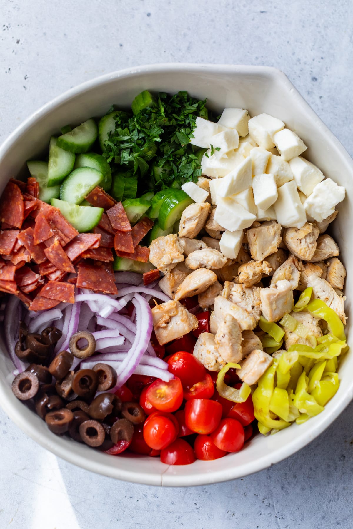 meats, cheeses, and vegetables for Italian pasta salad in a large white bowl.