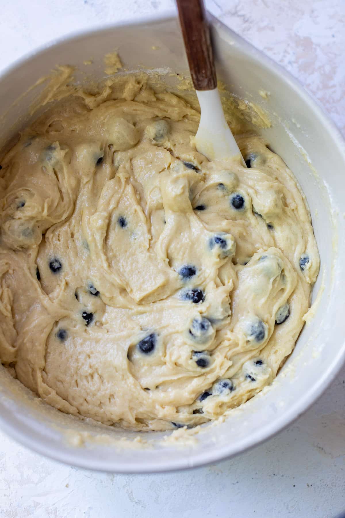 using a spatula to stir the batter for lemon blueberry cake in a large white bowl.