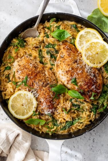 a skillet full of Lemon Chicken Orzo topped with fresh herbs and lemon slices.