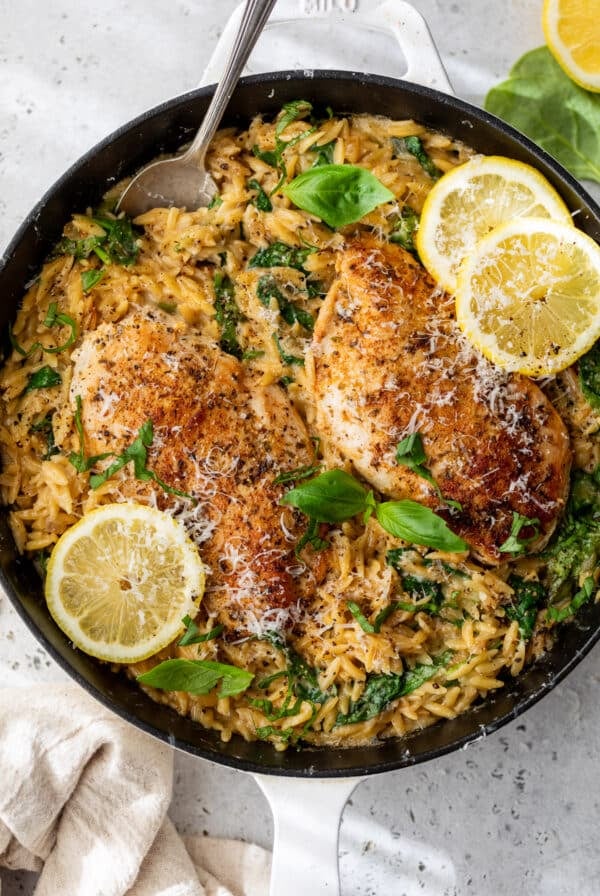 a skillet full of Lemon Chicken Orzo topped with fresh herbs and lemon slices.
