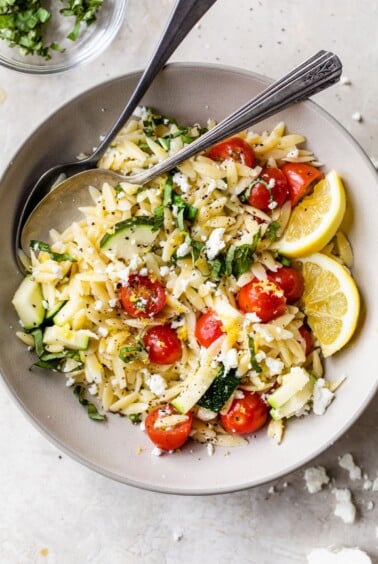 bowl with lemon orzo salad beside a small dish of chopped fresh basil