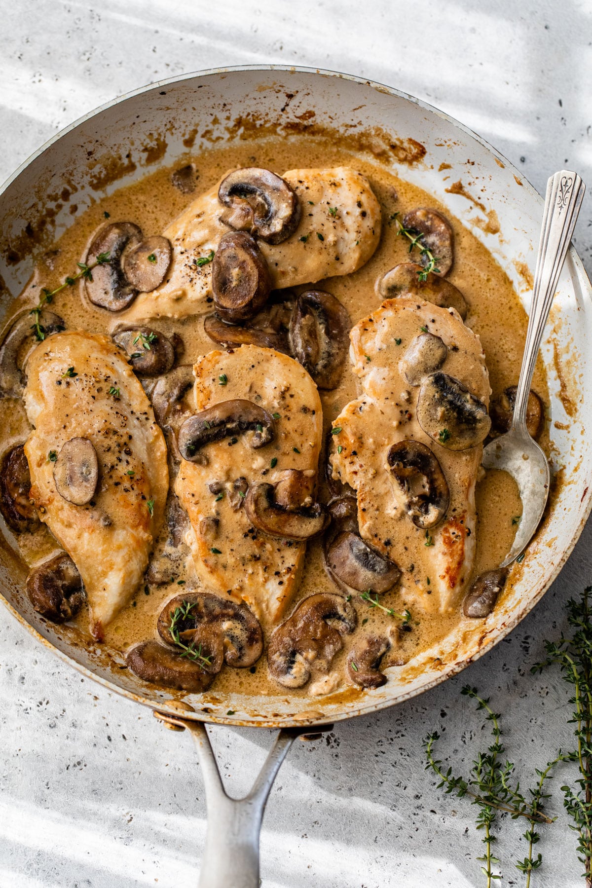 four chicken breasts in a skillet with a creamy mushroom sauce and fresh thyme
