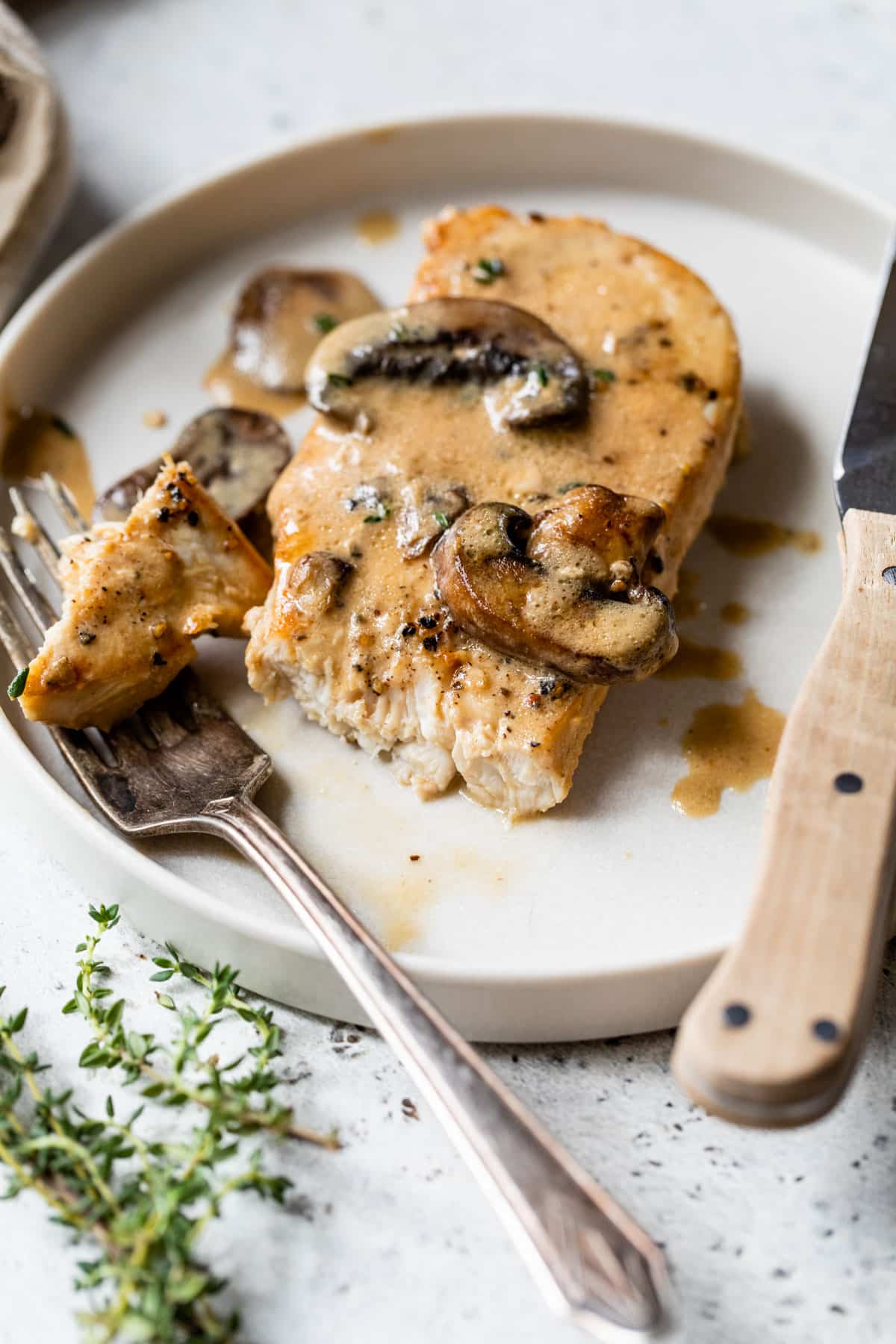 cooked chicken breast on a plate with mushroom sauce being cut with a fork and knife