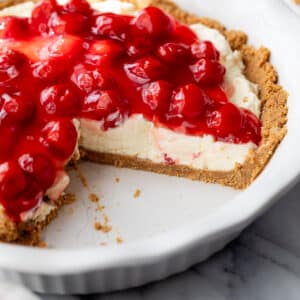 a whole pie topped with cherries with a slice taken out of it