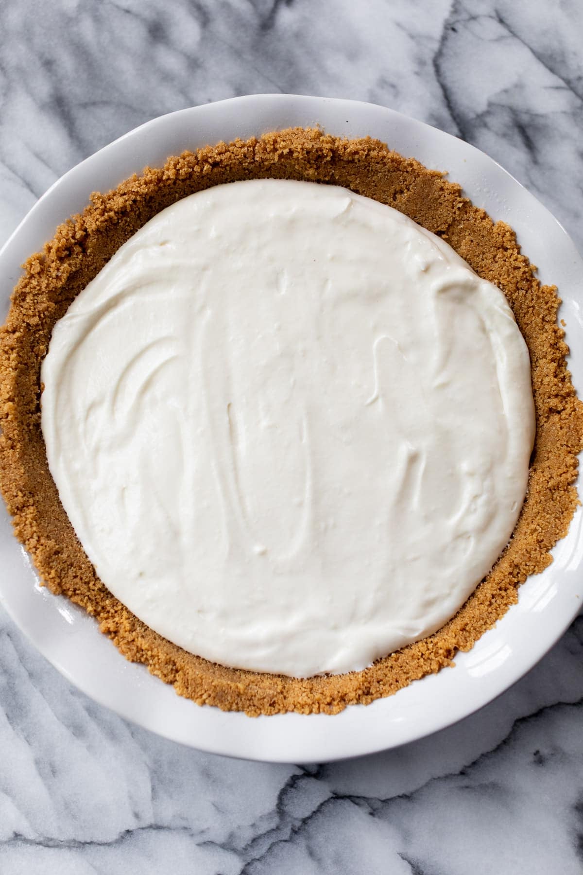 a whole pie with a graham cracker crust and creamy filling on a marble table