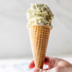 a hand holding an ice cream cone with 2 scoops of No Churn Pistachio Ice Cream.