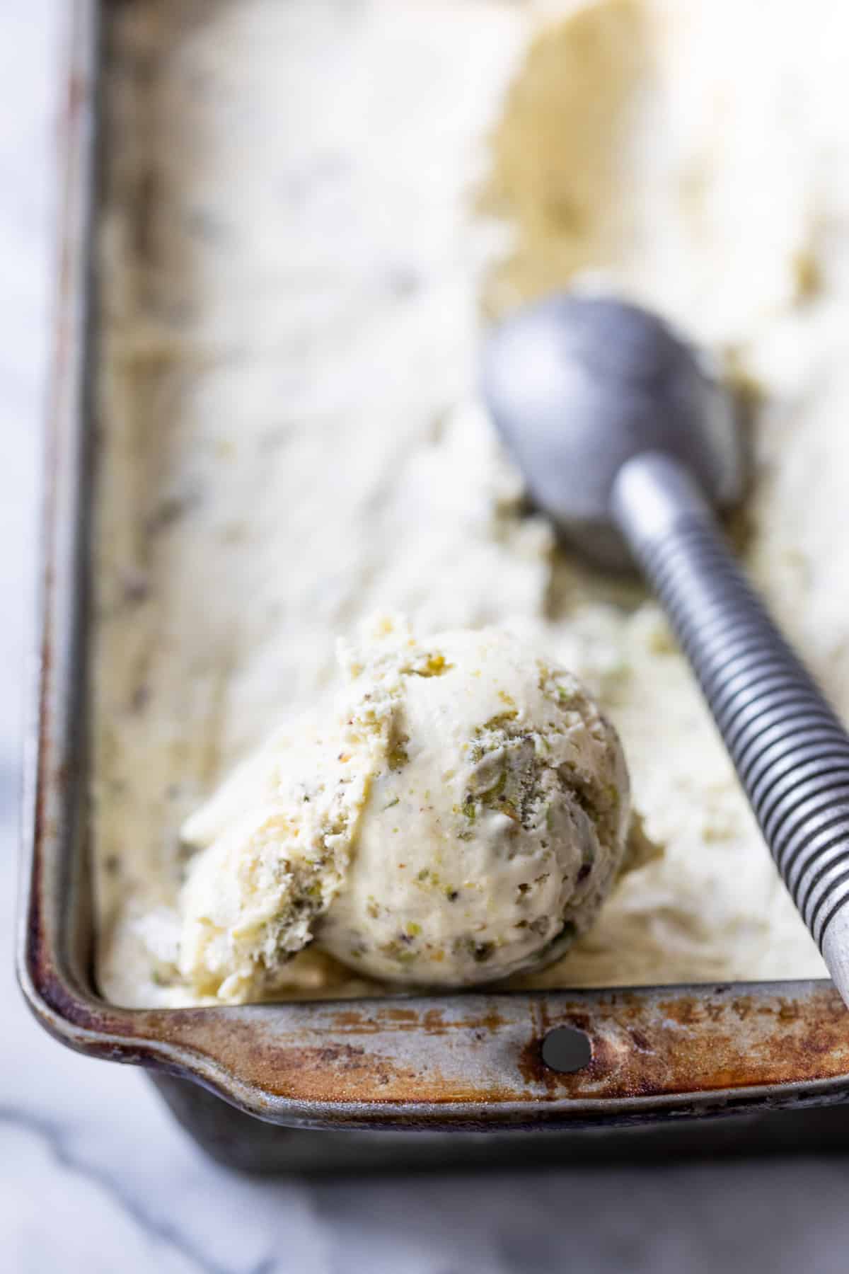 close up on an ice cream scoop, scooping No Churn Pistachio Ice Cream from a loaf pan.