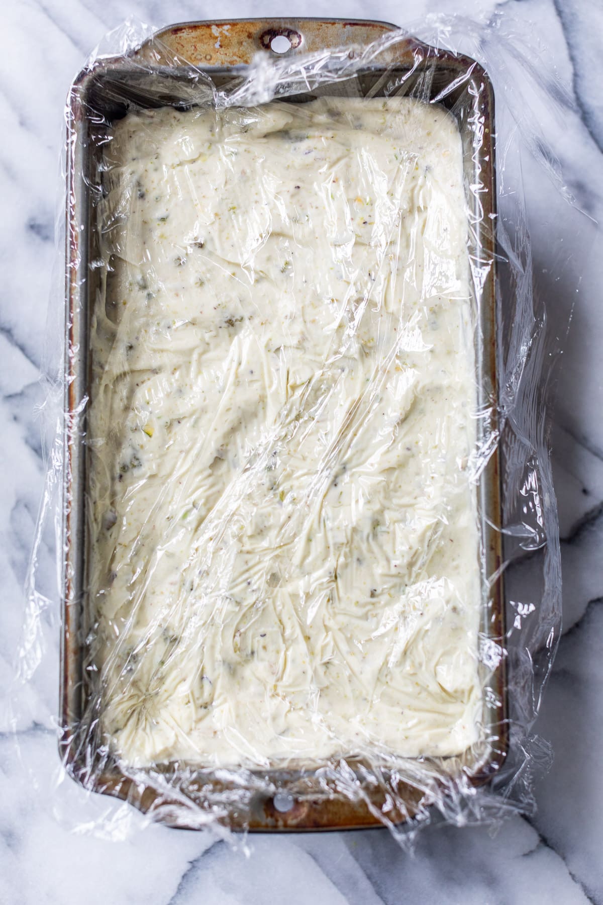No Churn Pistachio Ice Cream in a loaf pan, covered with a sheet of plastic wrap.