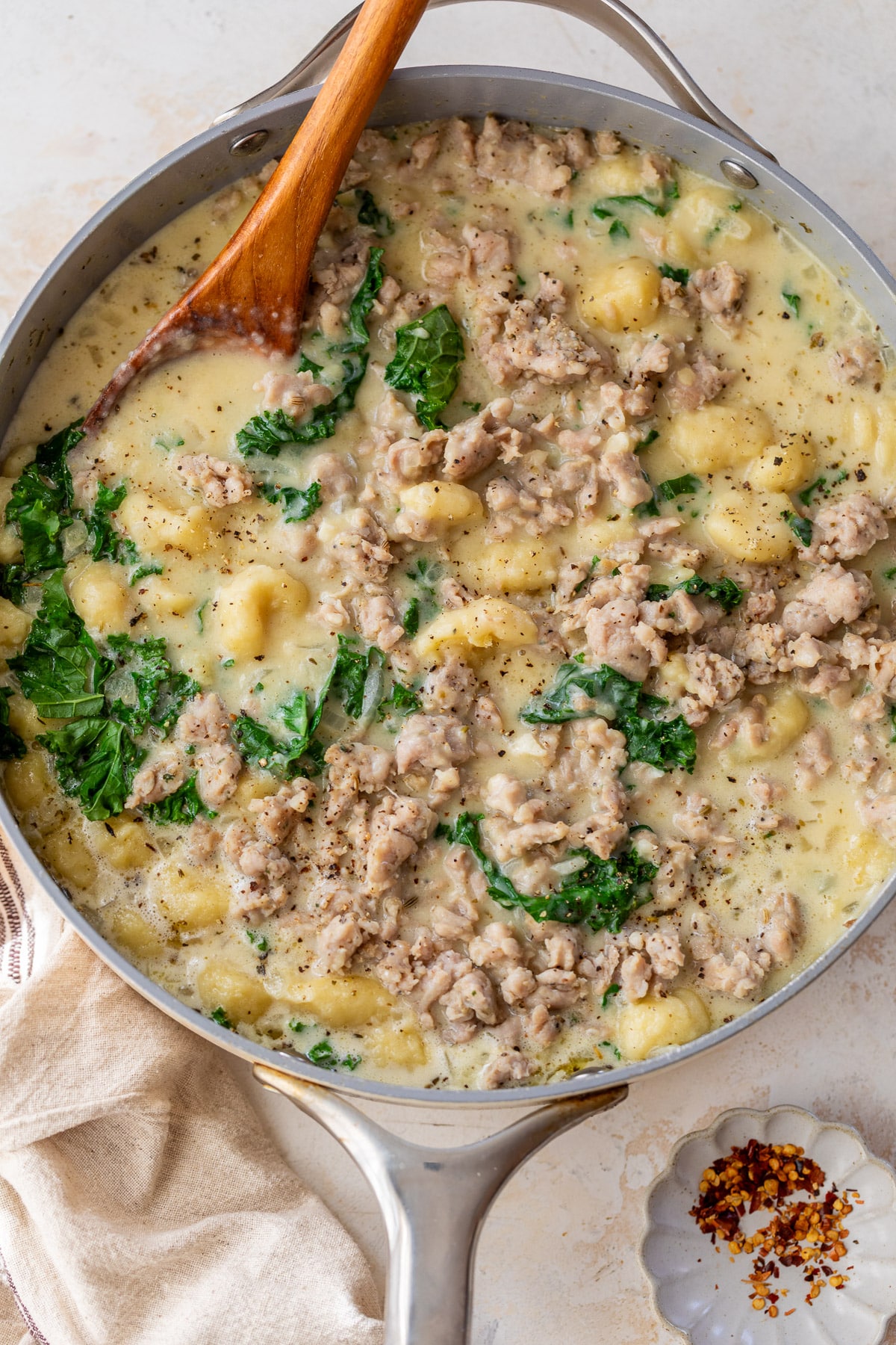 using a wooden spoon to stir Gnocchi with Sausage and Kale in a large skillet.