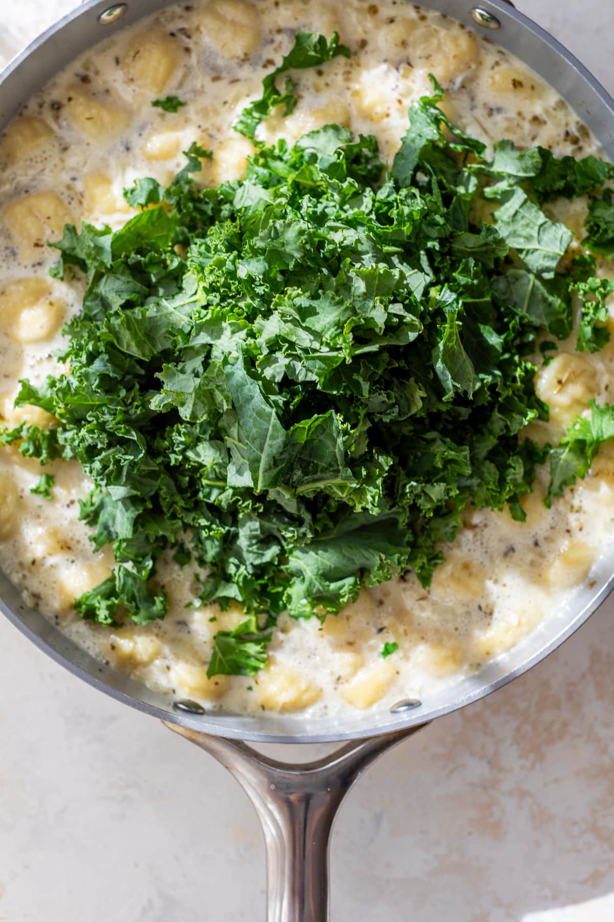 overhead view of chopped kale on top of Gnocchi with Sausage and Kale in a large skillet.