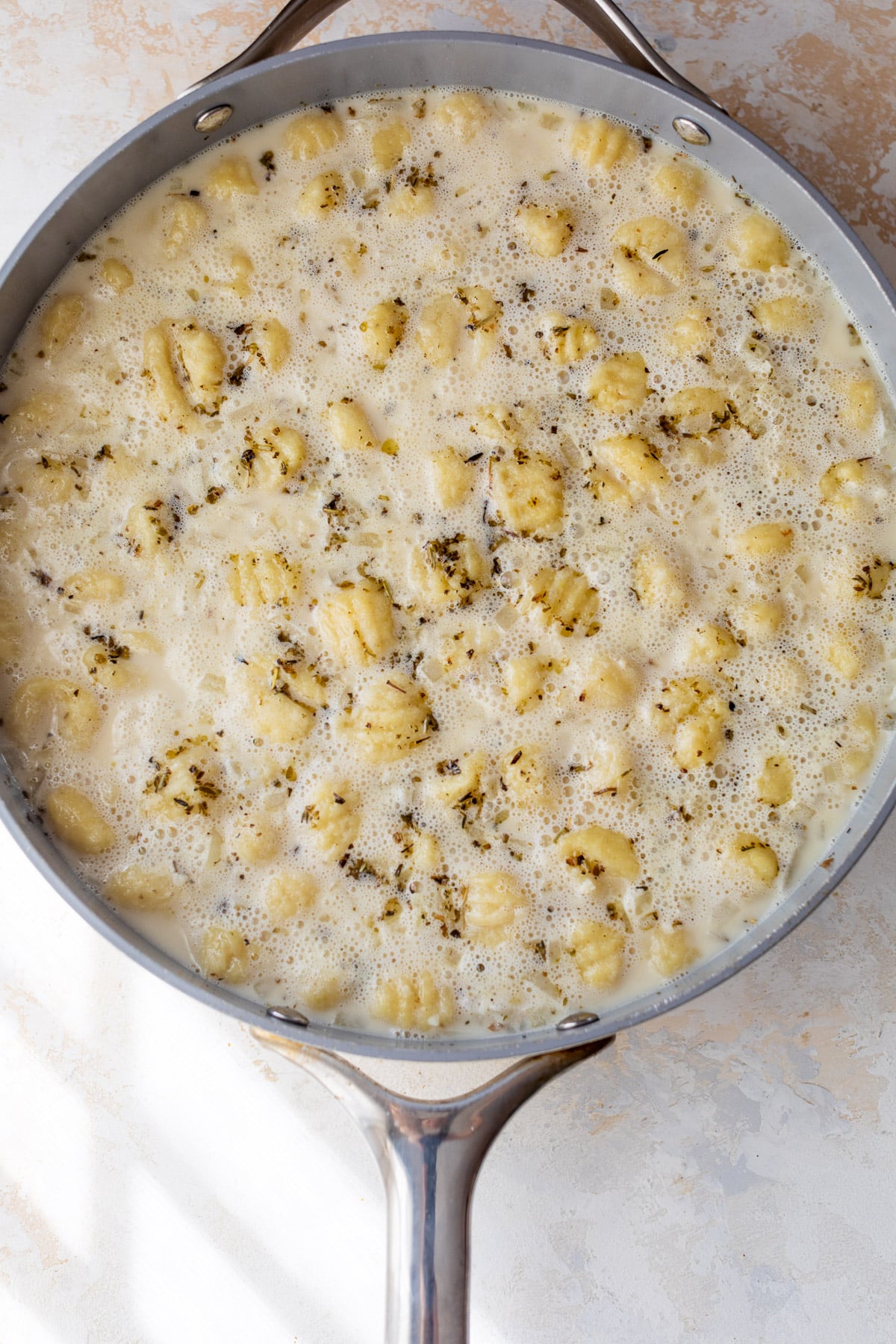 overhead view of gnocchi cooking in a broth and cream sauce for One Pot Gnocchi with Sausage and Kale.