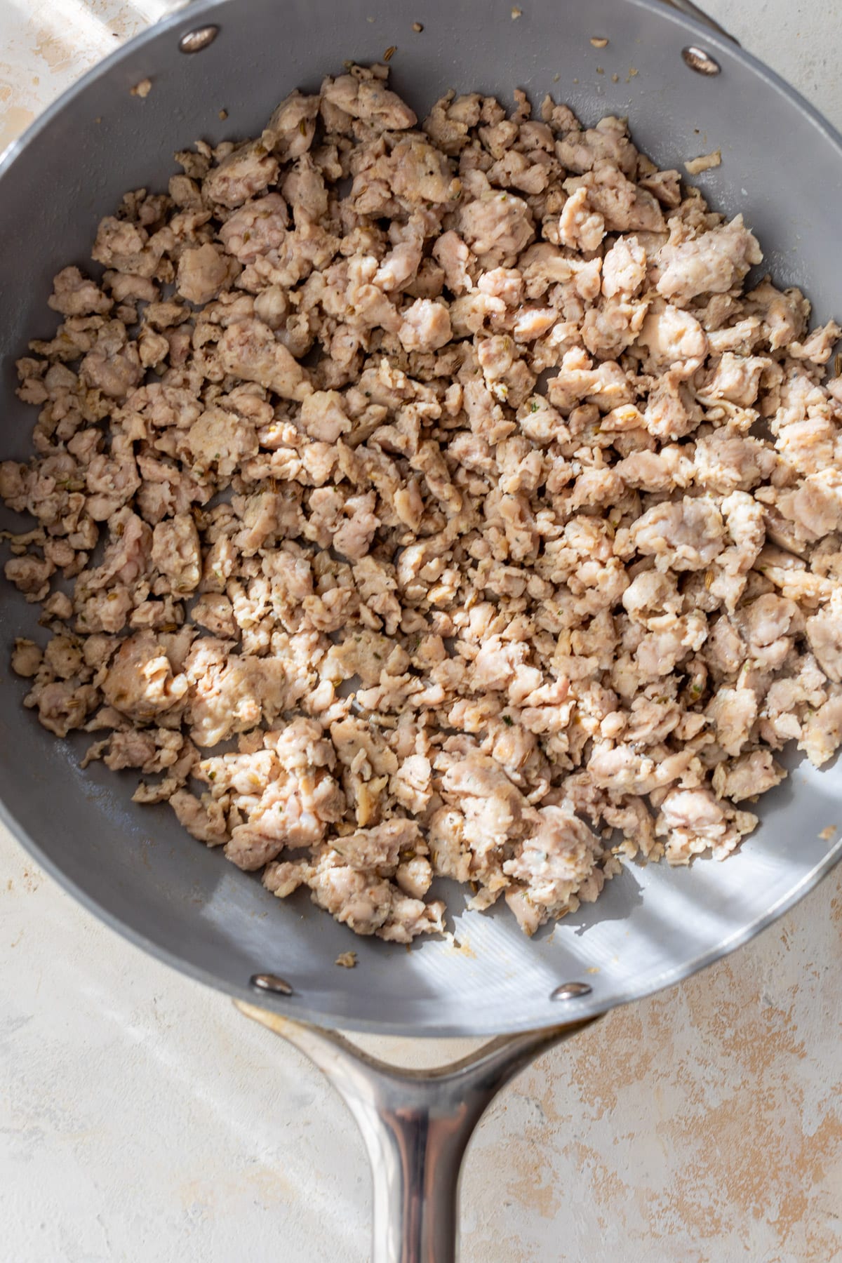 overhead view of crumbled chicken sausage cooking in a large skillet for One Pot Gnocchi with Sausage and Kale.