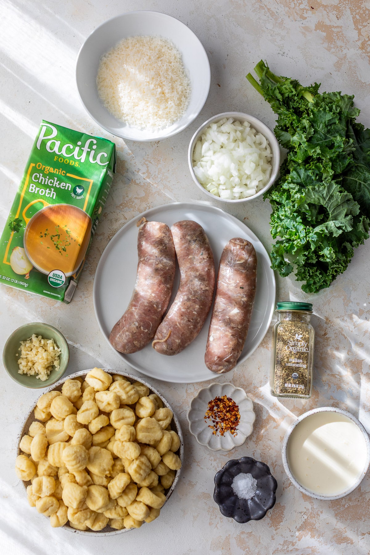 overhead view of the ingredients for One Pot Gnocchi with Sausage and Kale in individual white bowls.