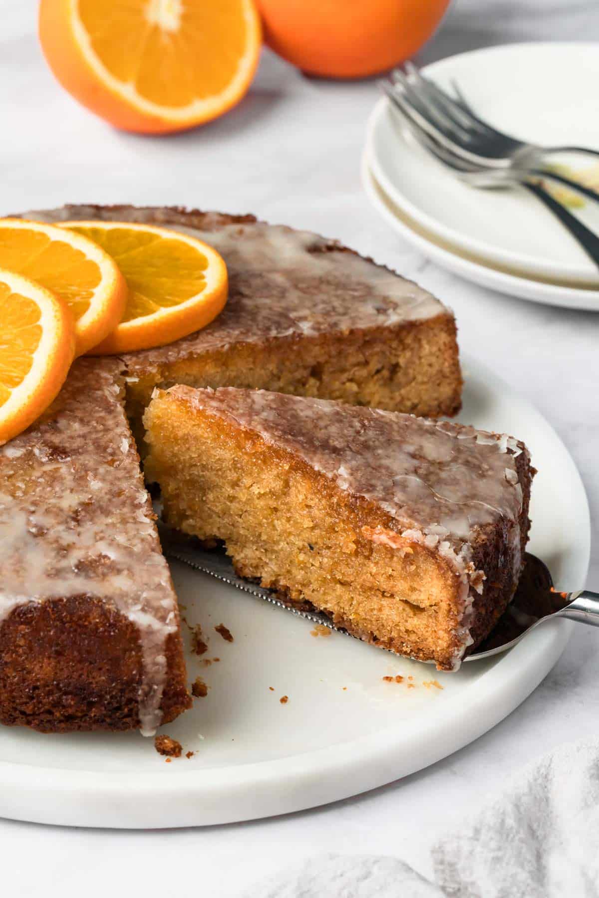 side view of a slice of orange cake being lifted from the cake on a white plate.