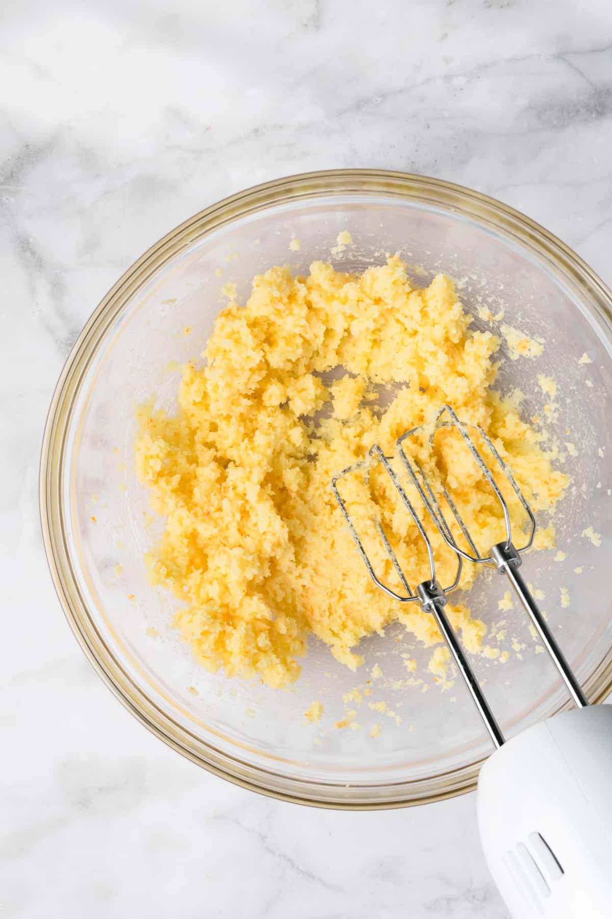 overhead view of butter and sugar being whipped together for orange cake batter in a glass bowl.