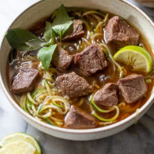 side view of paleo beef pho topped with Thai basil and lime wedges in a bowl.