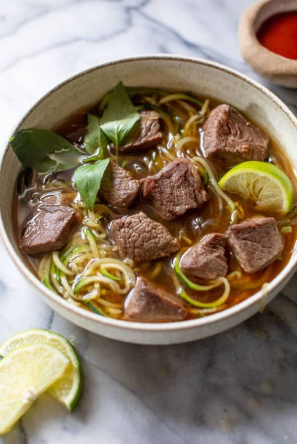 side view of paleo beef pho topped with Thai basil and lime wedges in a bowl.