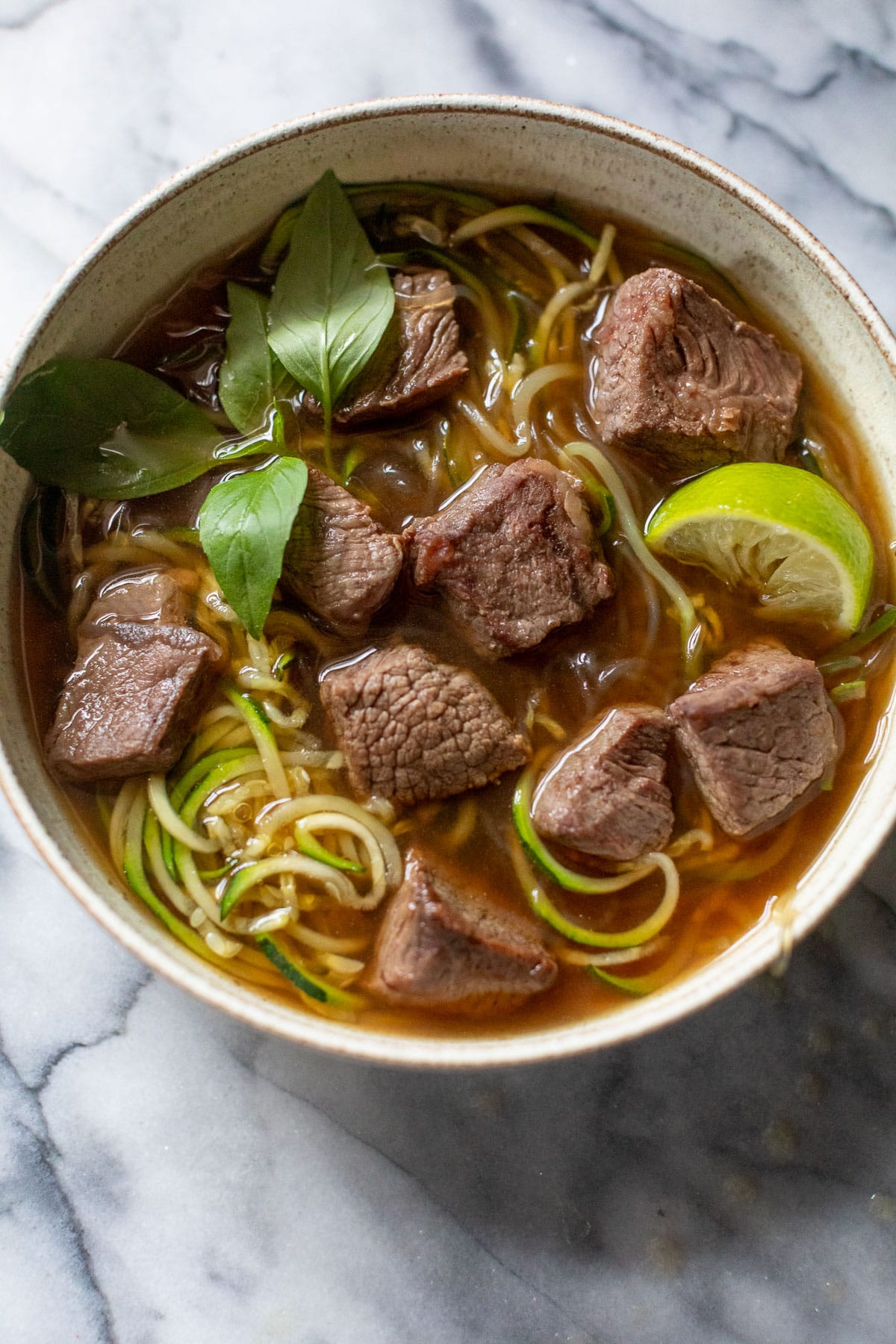 overhead view of paleo beef pho topped with Thai basil and lime wedges in a bowl.