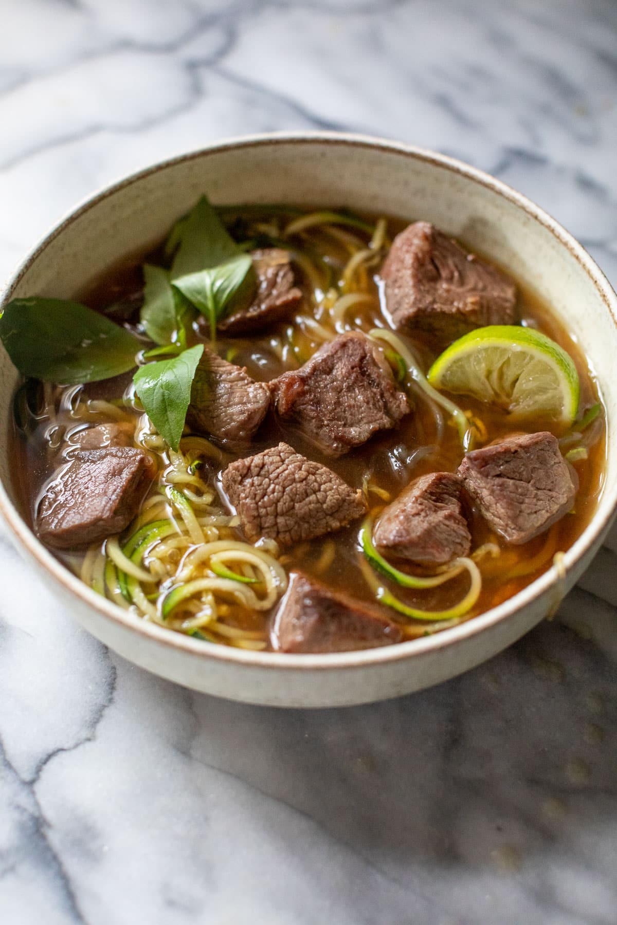 side view of paleo beef pho topped with Thai basil and lime wedges in a bowl.