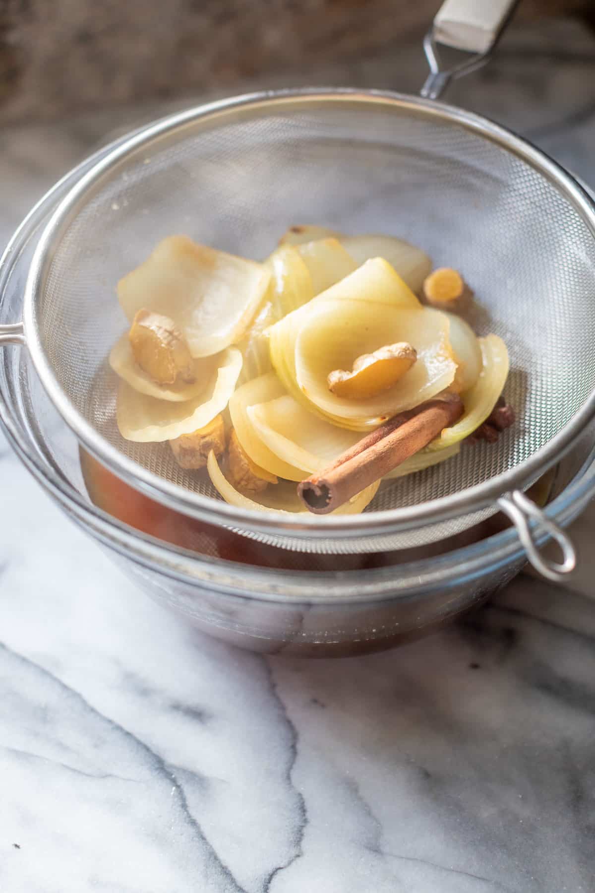 strained aromatics and spices in a fine mesh strainer overtop of a bowl of paleo beef pho broth.