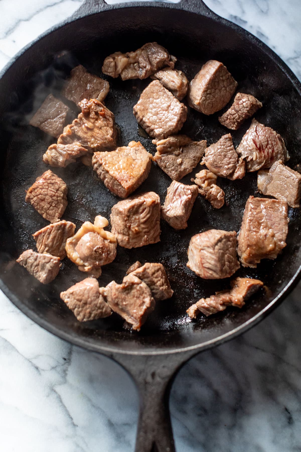 overhead view of cooked beef pieces in a black skillet.
