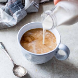 someone pouring coffee creamer into a mug of coffee