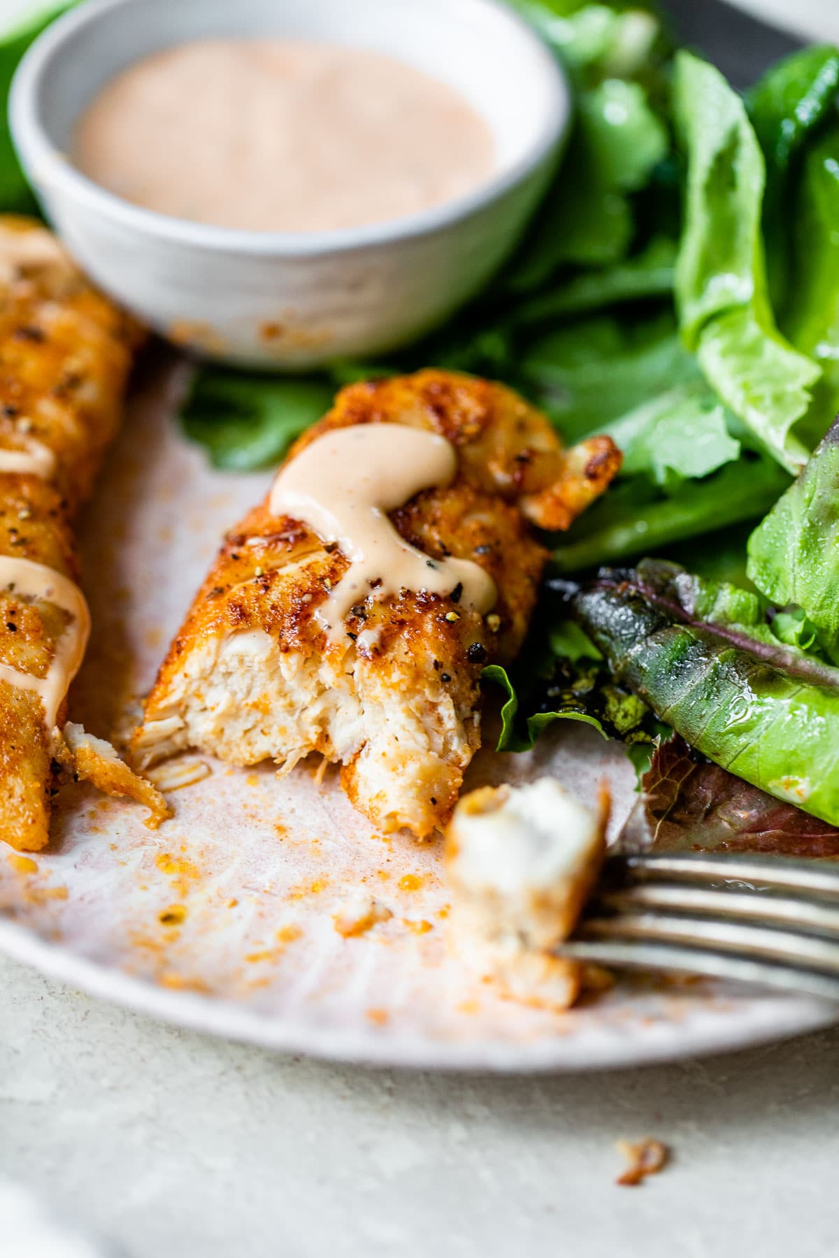 cut chicken tender beside mixed greens on a platte