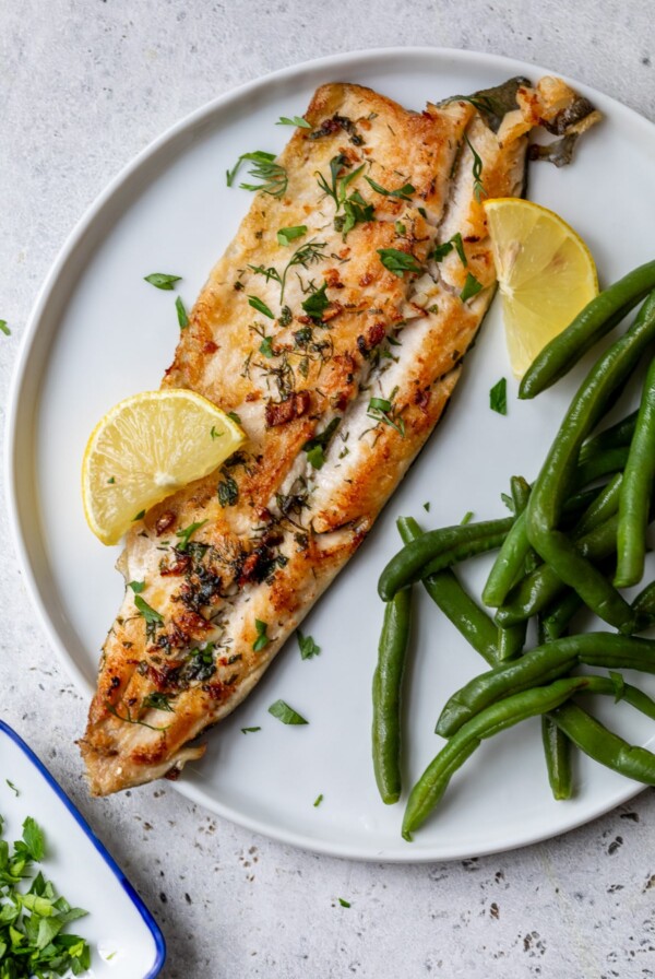 pan-fried trout on a plate with green beans and lemon wedges