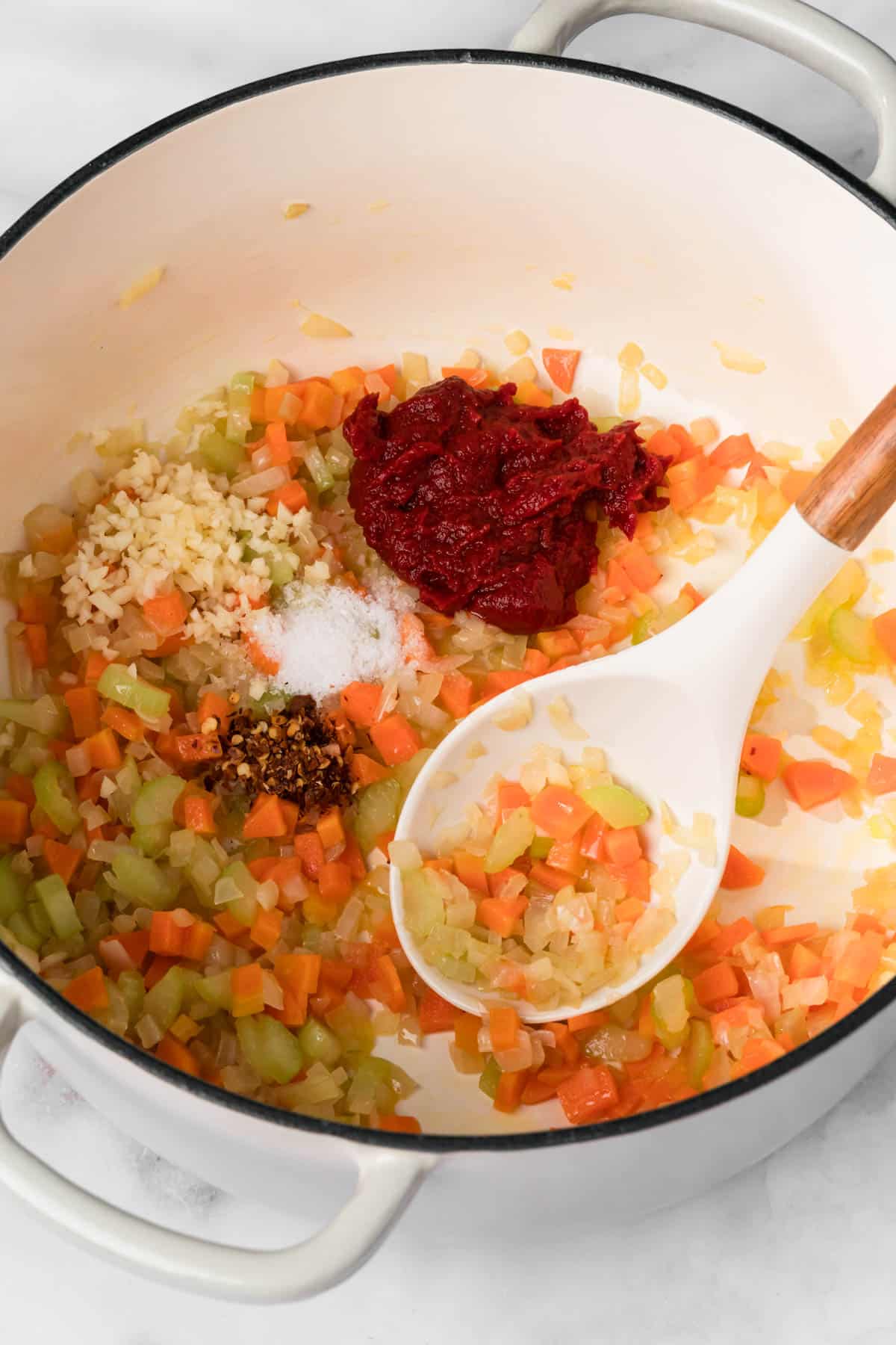 overhead view of a white spoon stirring cooked vegetables in a pot for pasta e ceci.