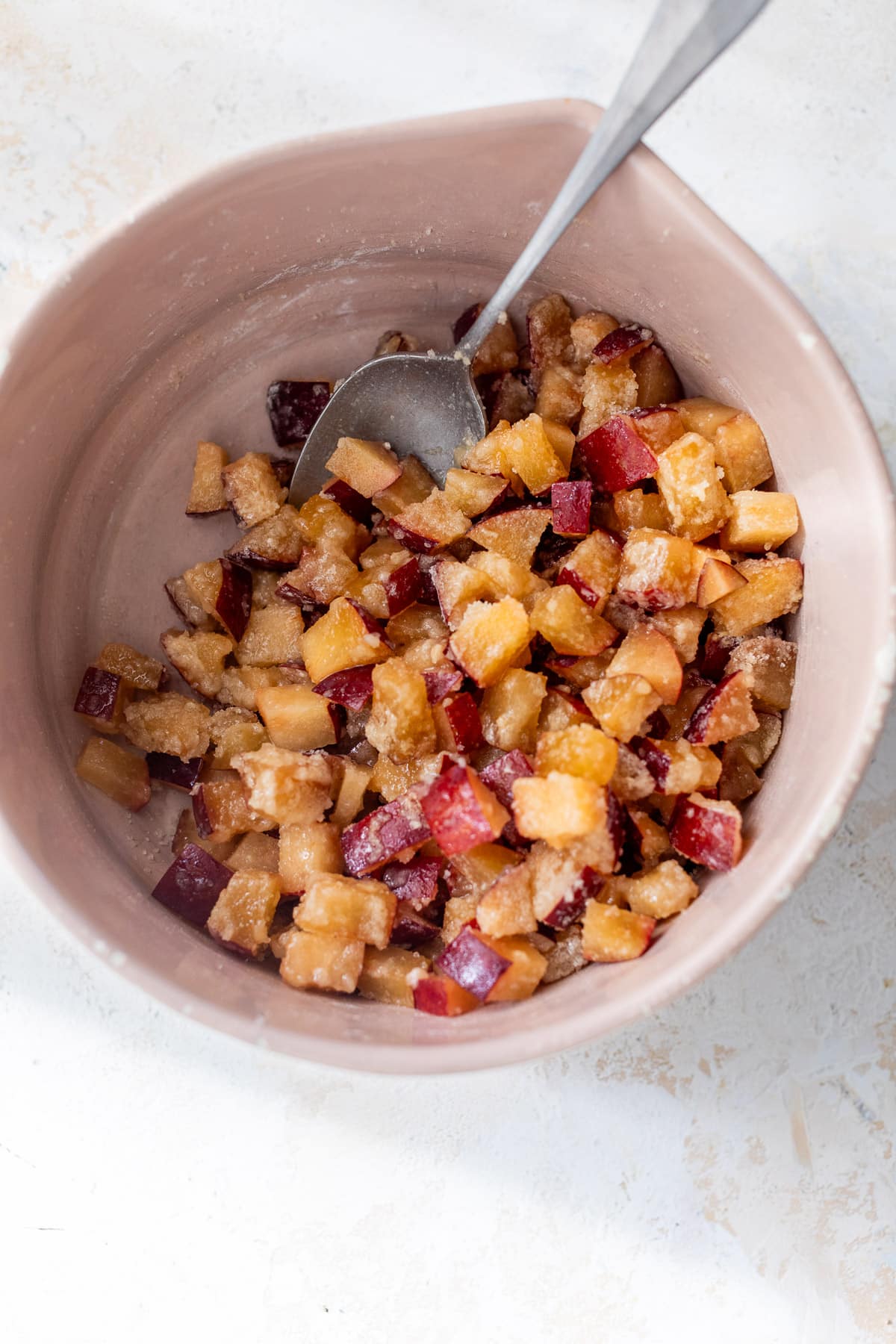 using a spoon to stir the plum filling for plum bars in a pink bowl.