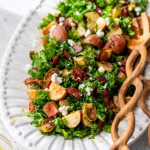 wooden salad tongs next to a potato brussels sprouts salad on a large white platter.