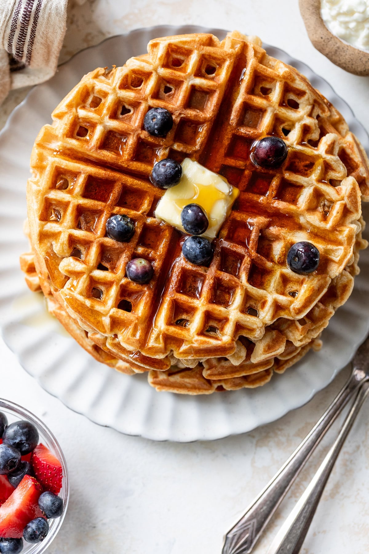 overhead view of a stack of protein waffles with butter, maple syrup, and blueberries on top.