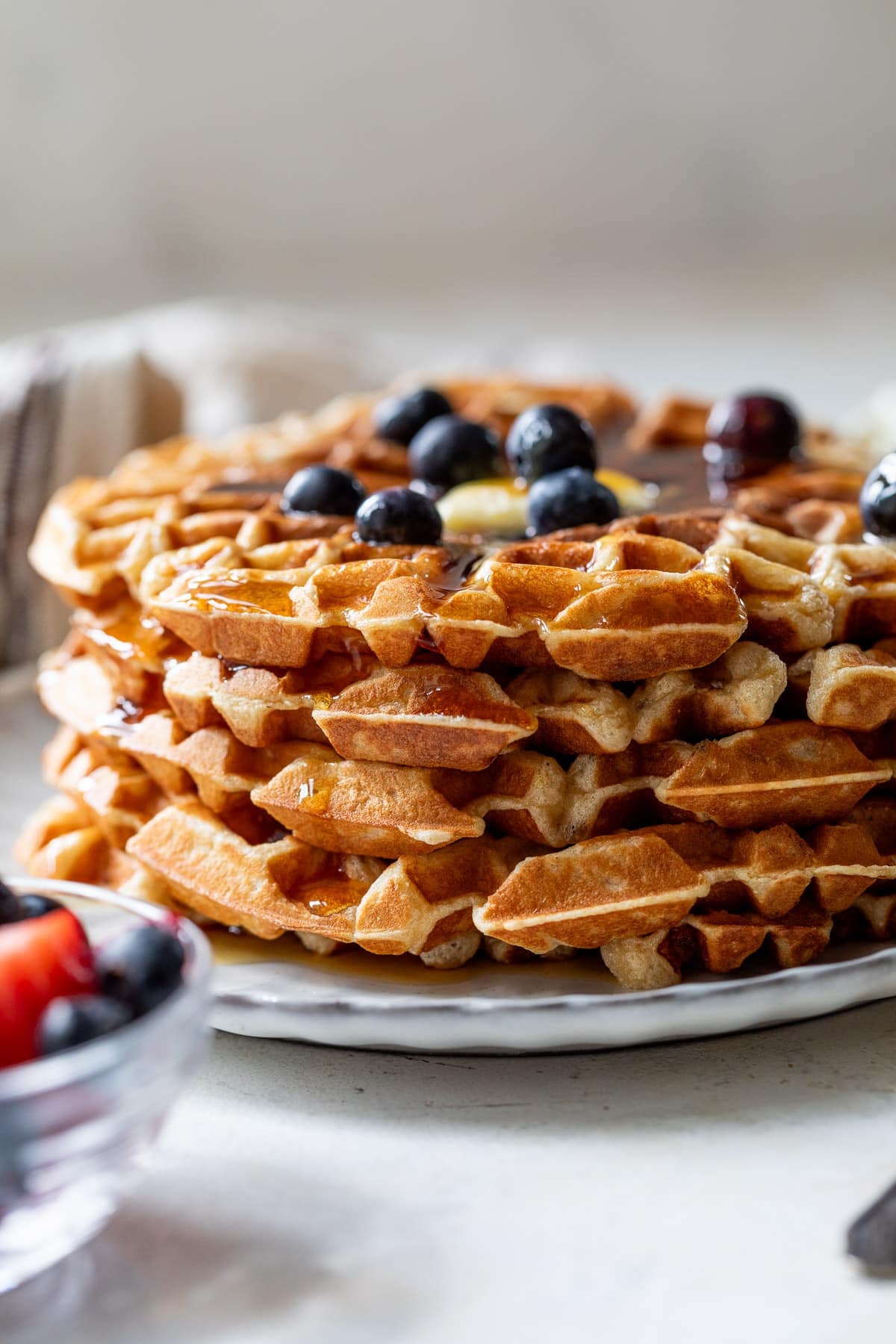 side view of a stack of protein waffles with butter, maple syrup, and blueberries on top.