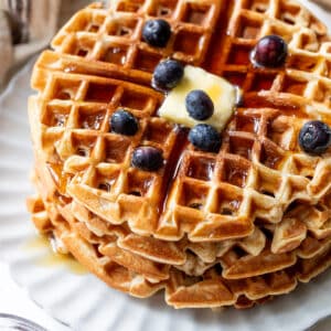 overhead view of a stack of protein waffles with butter, maple syrup, and blueberries on top.