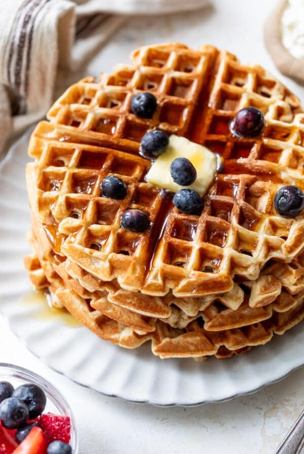overhead view of a stack of protein waffles with butter, maple syrup, and blueberries on top.
