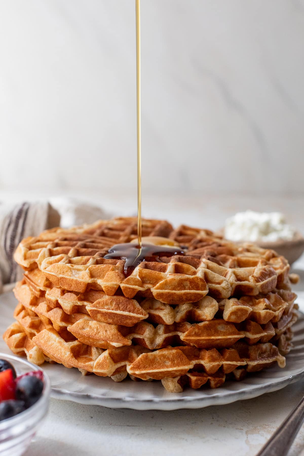 drizzling maple syrup over a stack of protein waffles.