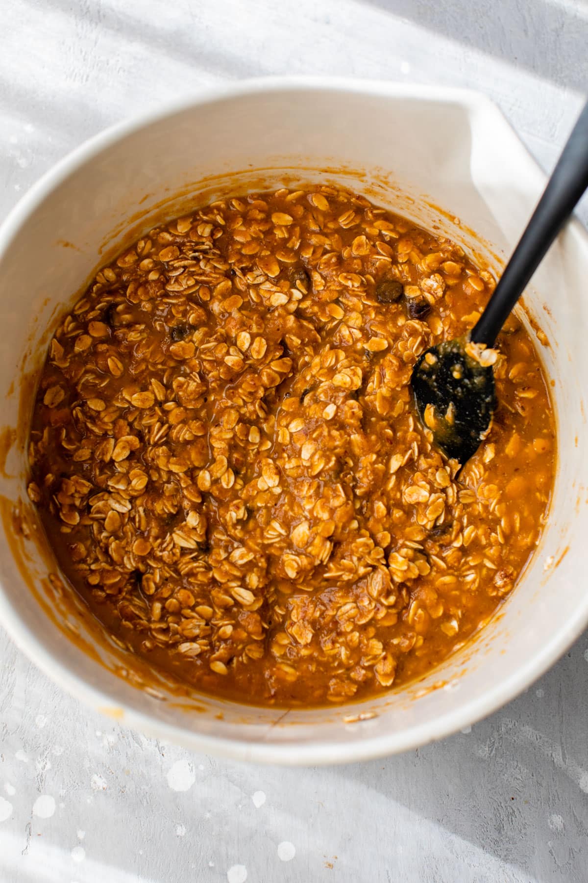 oats added to wet ingredients in a bowl with a spatula