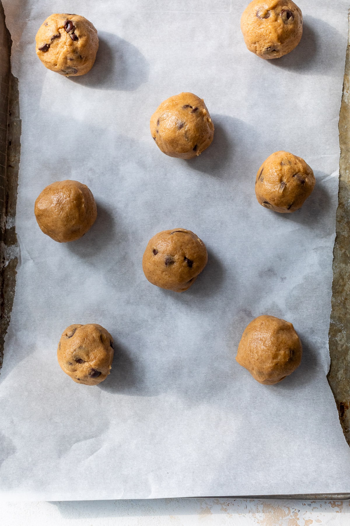 overhead view of rolled pumpkin chocolate chip cookie dough balls on a parchment-lined baking sheet.