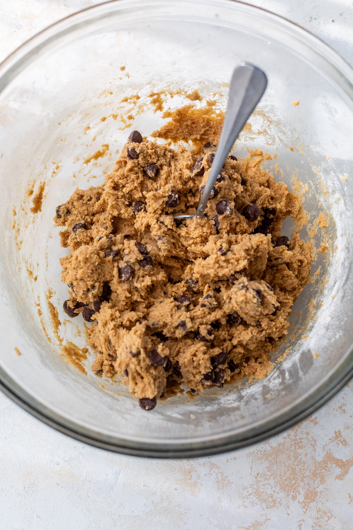 a spoon in a batch of pumpkin chocolate chip cookie dough in a glass bowl.