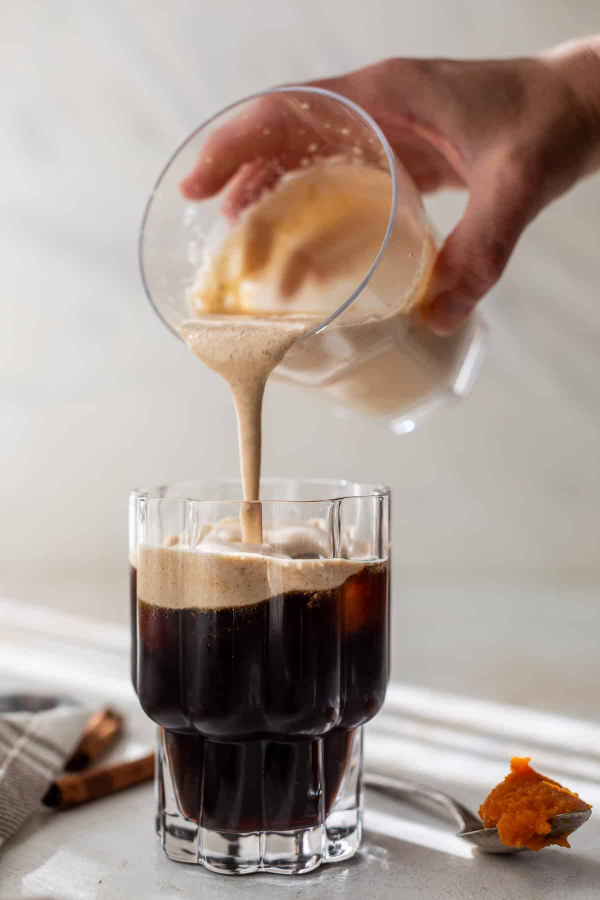 a hand pouring pumpkin creamer into a glass of cold brew.